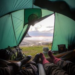 People camping outdoors in a tent in a region with mountains and lakes, on a vacation trip exploring nature and its beauties.